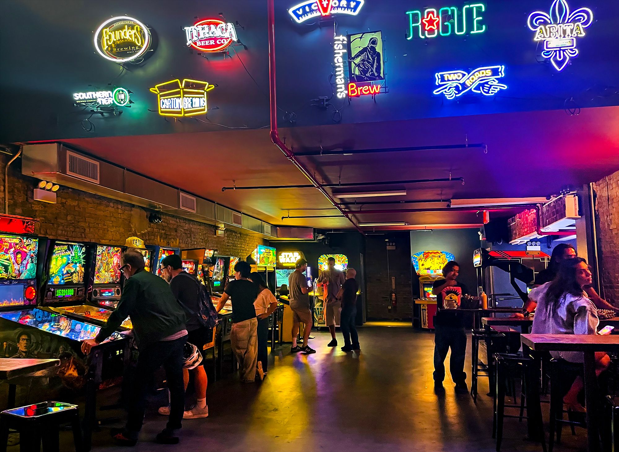 Young people playing pinball machines in arcade setting