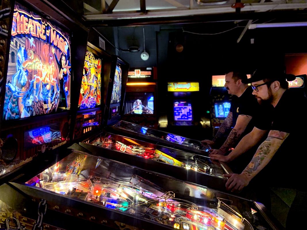 Young people playing pinball machines in arcade setting